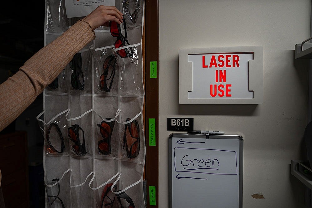 Person storing safety glasses next to a Laser In Use sign 