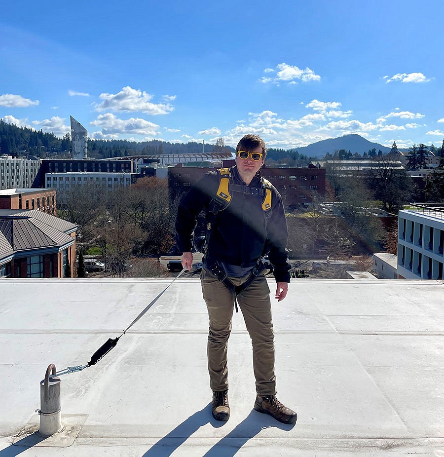 Person on roof wearing a harness and attached to an anchor for fall protection. 