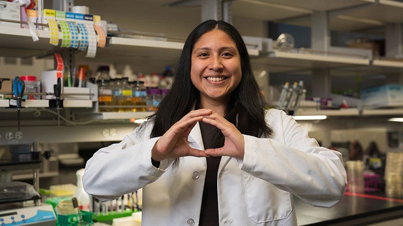 UO Researcher wearing a white lab coat with hands forming an O