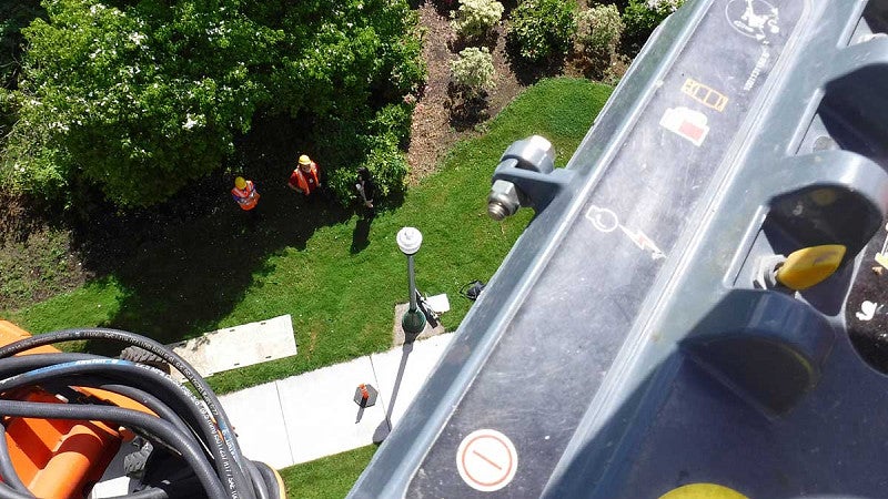 View looking down from a raised aerial lift with two people in hard hats and safety vests below. 