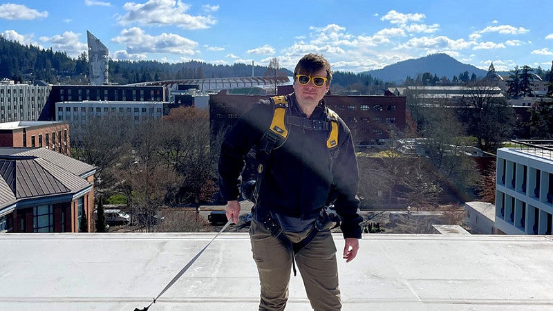 Person on roof wearing a harness and attached to an anchor for fall protection. 