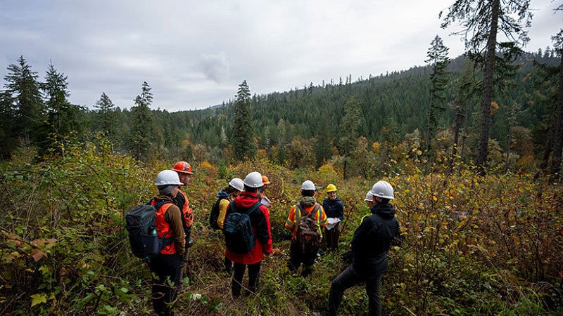 A group of researchers in the field wearing hard hats, vests, and backpacks