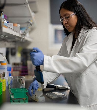 Researcher wearing white lab coat, gloves, and protective goggles working in lab