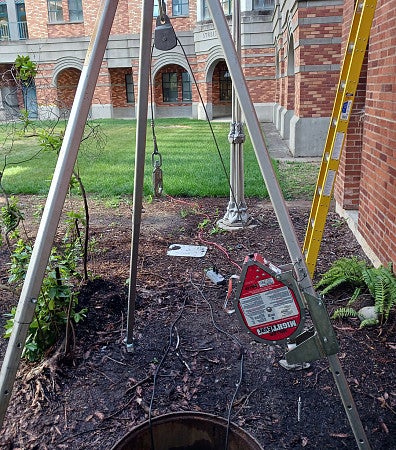 A rescue tripod is over an open manhole where employees will enter and work